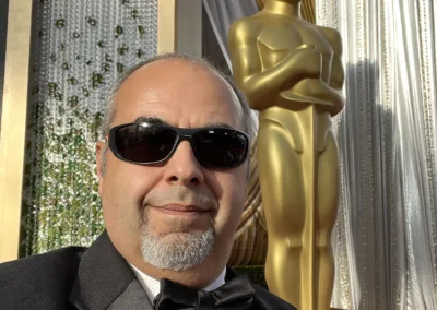 A man wearing sunglasses and a tuxedo in front of an oscar statue.