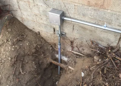 A water meter in the ground next to a brick wall.